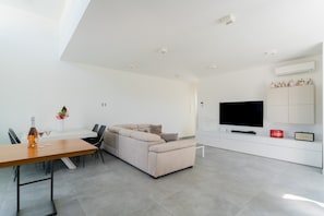 Ein modernes Wohnzimmer mit Sofa, Esstisch und Fernseher.