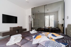 A modern bedroom with a bed, a flat-screen TV, a glass wardrobe, and a bench. - Villa Ginevra: Exclusive Luxury and Wellbeing Near Otranto (Otranto)