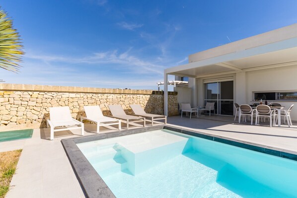 A swimming pool with lounge chairs, a stone wall, and a patio area with outdoor furniture. - Villa Ginevra: Exclusive Luxury and Wellbeing Near Otranto (Otranto)