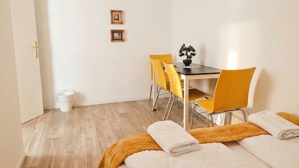 Une chambre d’hôtel avec un lit, une table et des chaises, une plante en pot et une poubelle.