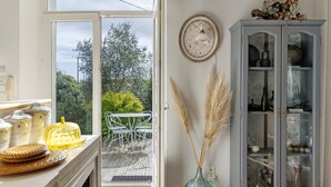 Una cocina con vistas al exterior, un comedor con sillas, un armario con puertas de vidrio y un jarrón con plantas secas.