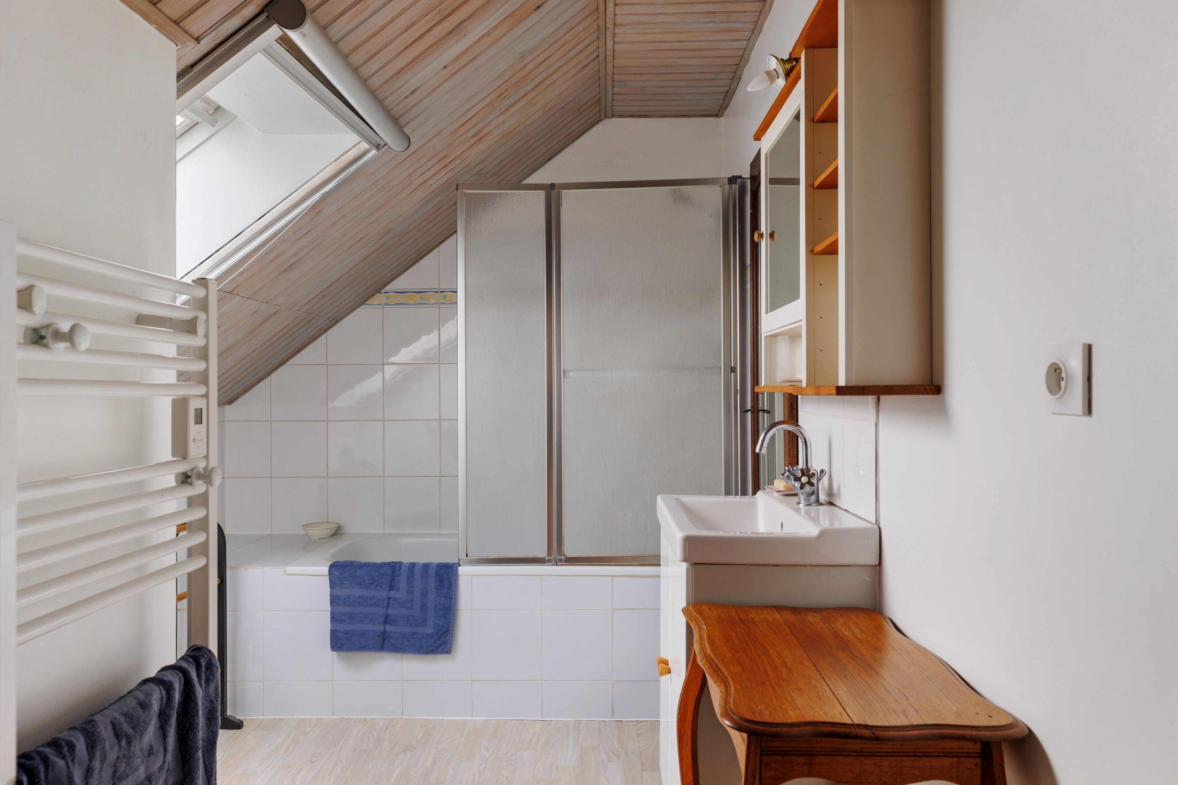Une salle de bain moderne avec une lucarne, une douche, un lavabo et une table en bois.