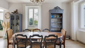 Un comedor con una mesa redonda, seis sillas, un aparador azul con puertas de cristal y una araña.