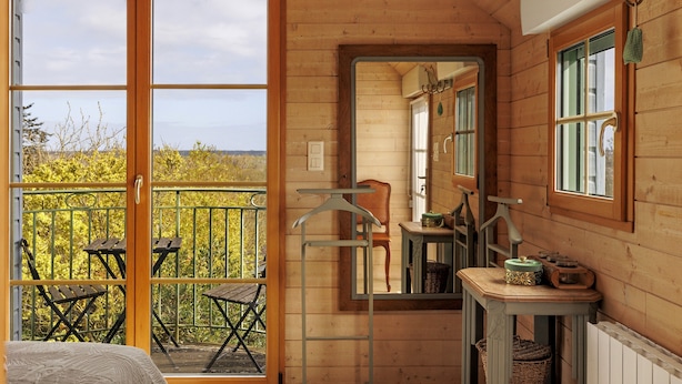Una cabaña de madera con balcón, un espejo y una pequeña mesa con objetos encima.