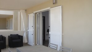 A room with a table, two chairs, a sofa, and a sliding door leading to another room. - Modern T3 Apartment in Calvi with Terrace – Available from August 22, Discounted Rates (Calvi)