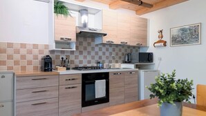 A modern kitchen with a gas stove, microwave, and a built-in oven. There is a sink with a faucet, a coffee maker, and a plant on the countertop. - Cozy studio apartment in the Dolomites (Tesero)