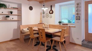 A cozy dining area with a wooden table and chairs, a hanging light fixture, and decorative plates on the wall. - Cozy studio apartment in the Dolomites (Tesero)