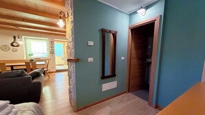 A room with a wooden ceiling, a stone pillar, a mirror, a wooden door, and a bed. - Cozy studio apartment in the Dolomites (Tesero)