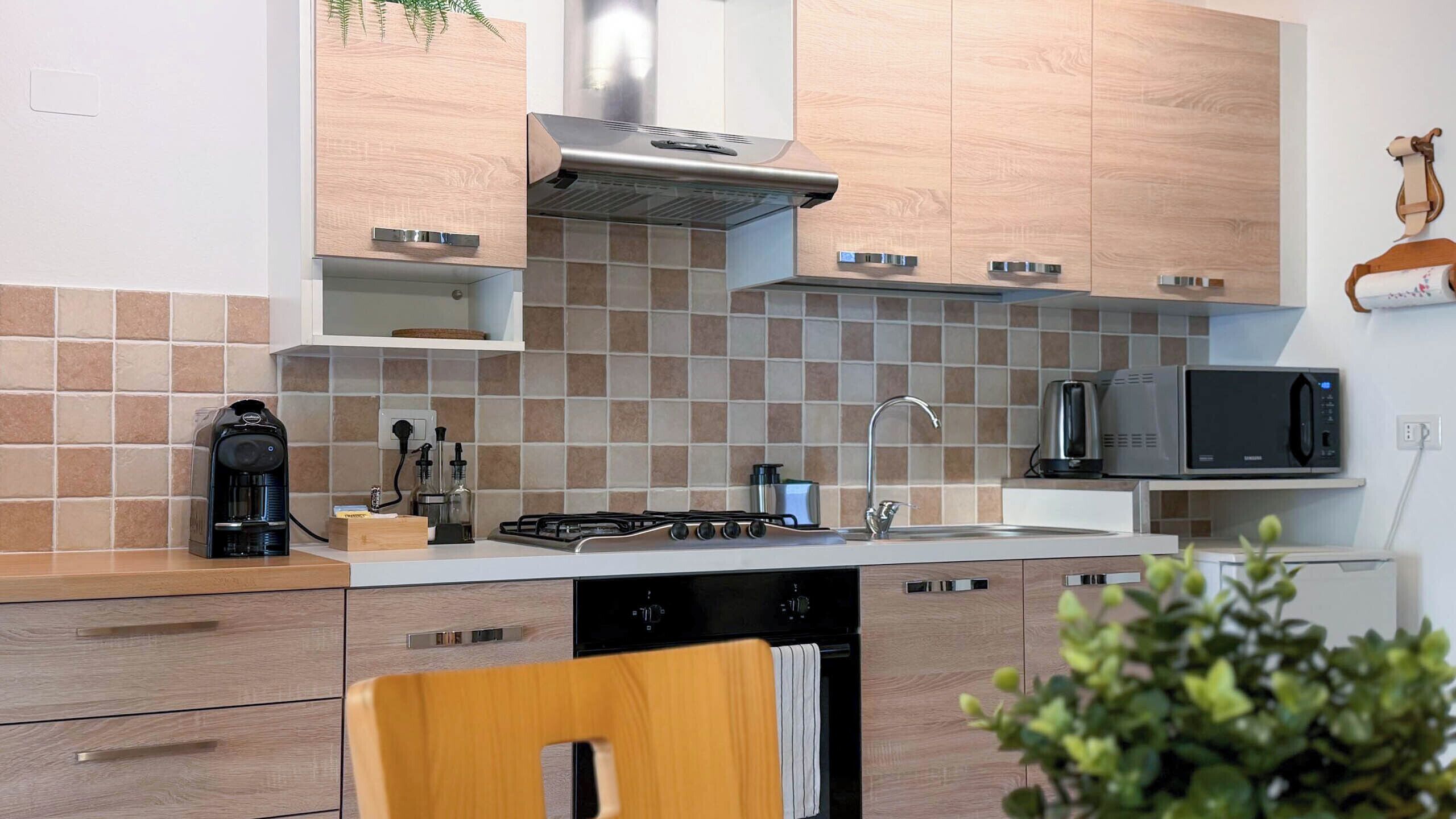 Une cuisine moderne équipée d’une cuisinière à gaz, d’un four à micro-ondes et d’un évier. On y trouve des armoires en bois et un pare-feu en carrelage.
