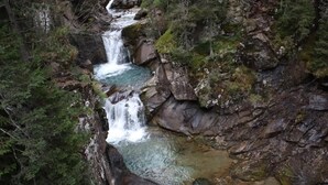 A waterfall cascading down a rocky cliff surrounded by dense forest. - Cozy studio apartment in the Dolomites (Tesero)