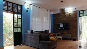 Un soggiorno con un divano grigio, un tavolino in legno, una TV montata su una parete in pietra e un balcone con ringhiera in legno.