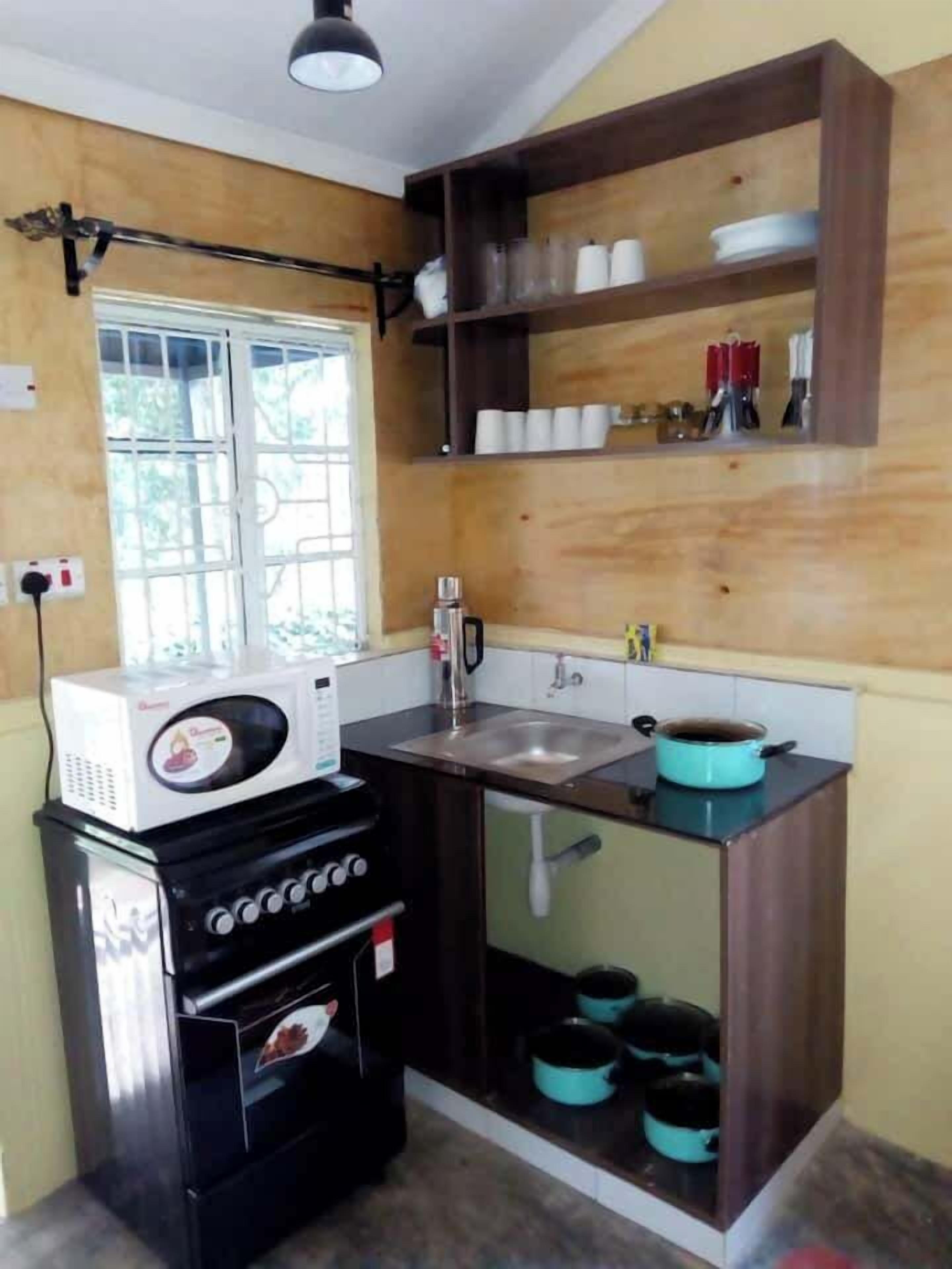 A compact kitchen with a microwave, stove, sink, and shelves above the counter.