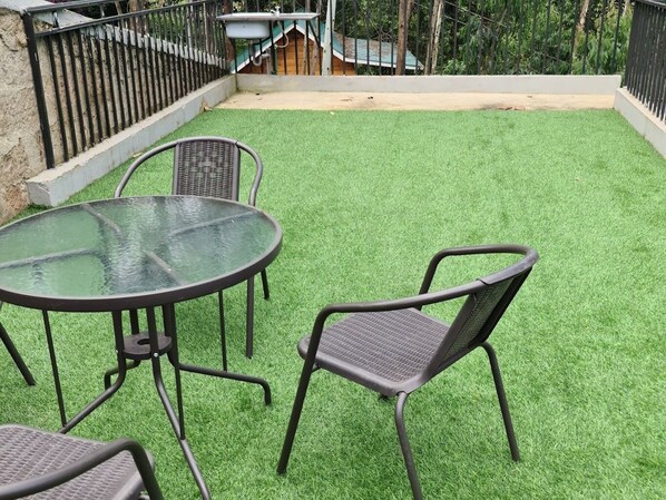 A patio with a round glass table and two chairs, surrounded by artificial green grass.
