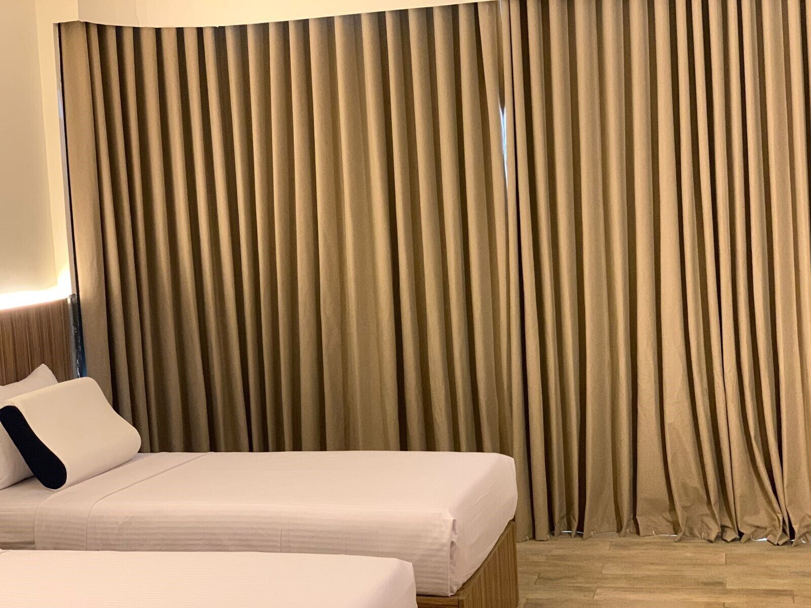 A hotel room with a bed, a nightstand, and a large window with curtains.