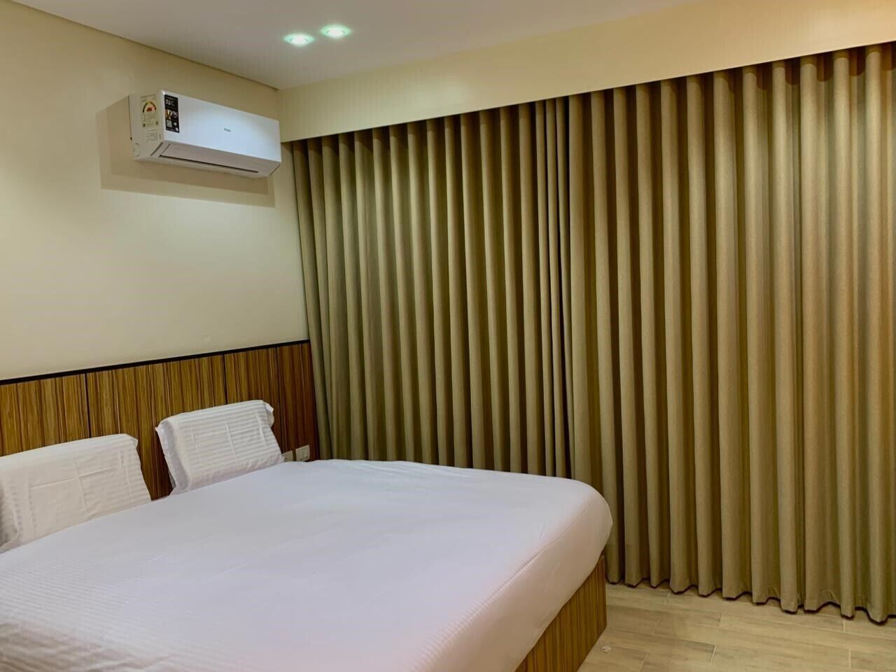 A hotel room with a large bed, a headboard, a wall-mounted air conditioner, and a set of curtains.