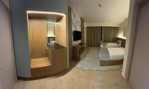 A modern hotel room with a curved seating area, a flat-screen TV, a bed with a white comforter, and a large window with curtains. - Tamaya (Tenth of Ramadan City)