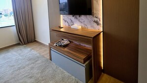 Moderni huone, jossa on seinään kiinnitetty litteänäyttöinen televisio, marmoriseinä, puinen konsolipöytä ja suuri ikkuna, jossa on verhot.