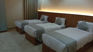 Habitación de hotel con tres camas, cabeceros de madera y alfombra de color claro.