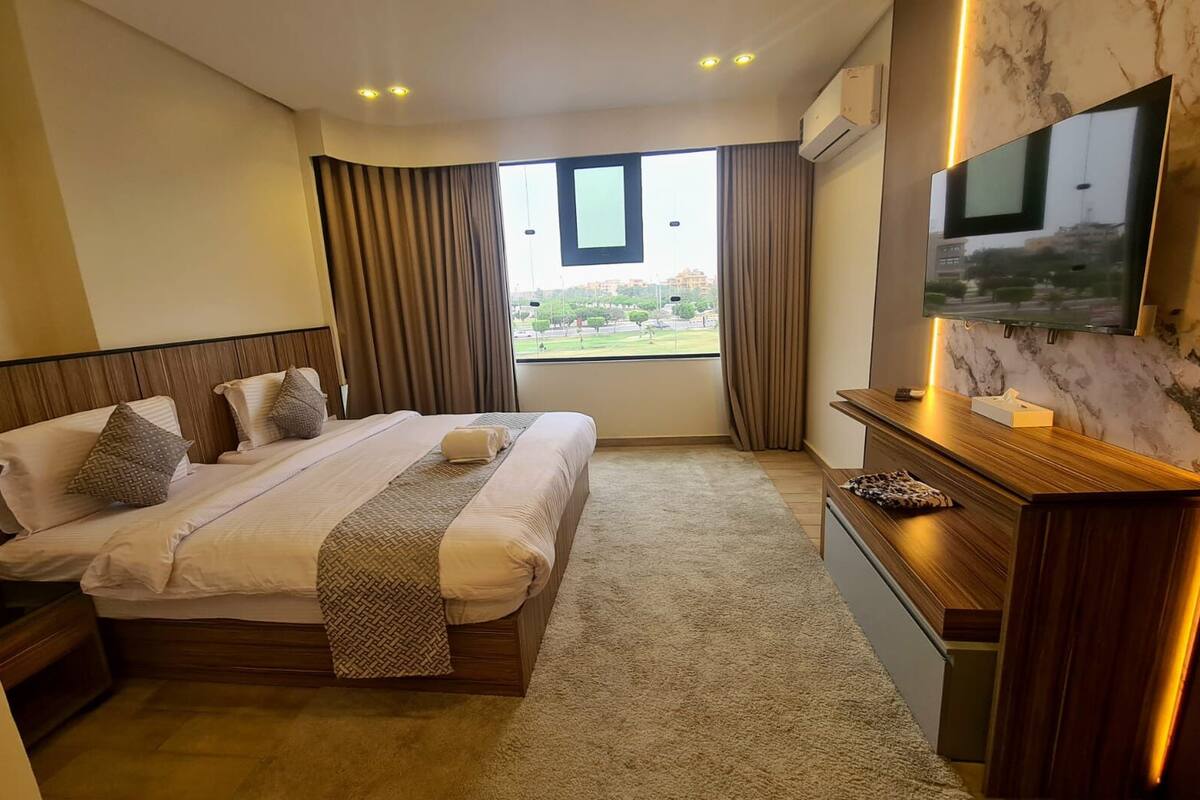 Ein Hotelzimmer mit einem großen Bett, einem Holzschrank, einem Flachbildfernseher und Blick ins Freie.