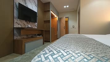 A modern hotel room with a large bed, a flat-screen TV mounted on a marble wall, wooden furniture, and a walk-in closet.