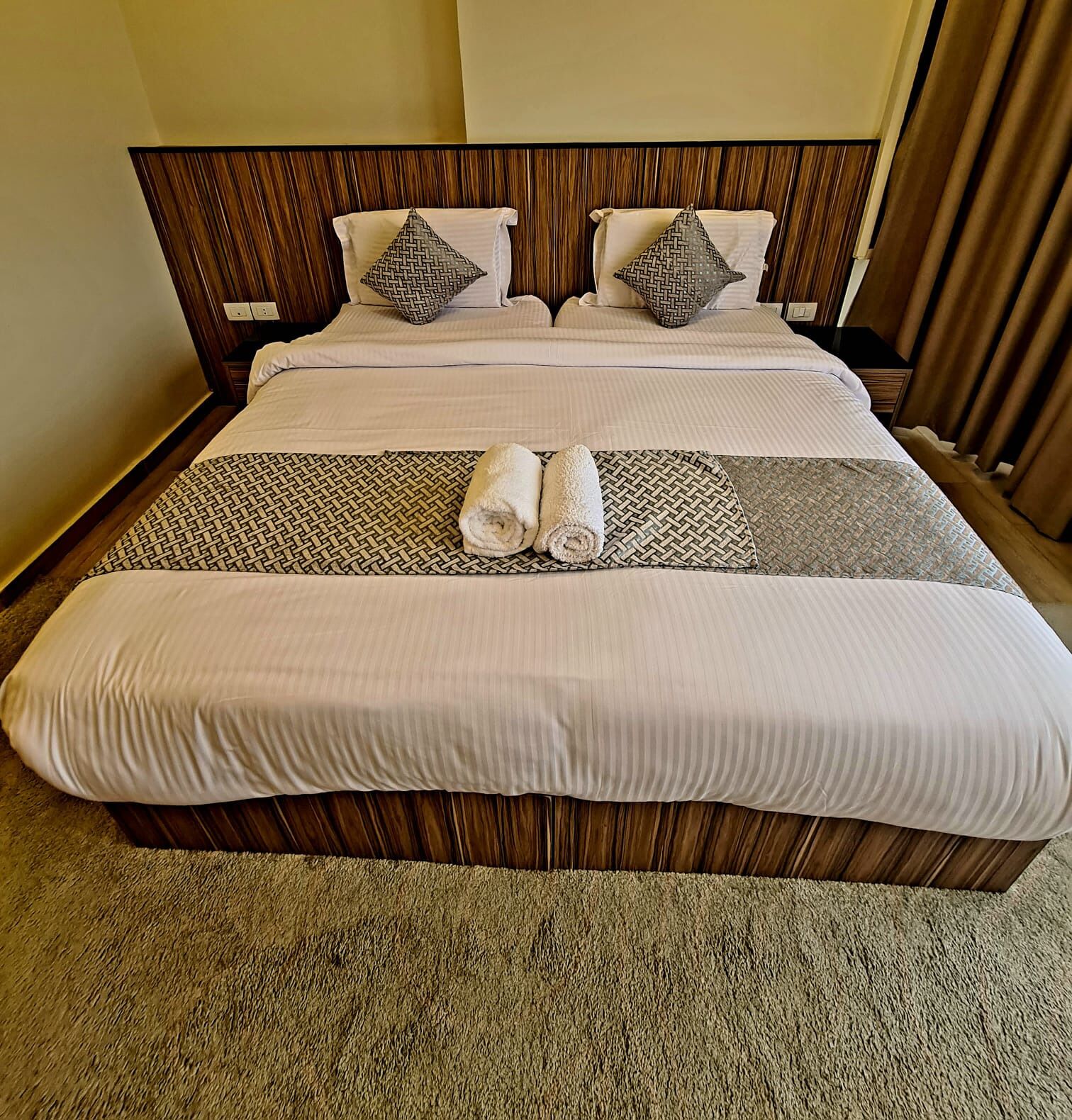 A neatly made bed with a striped bedspread, two pillows, and two rolled towels.