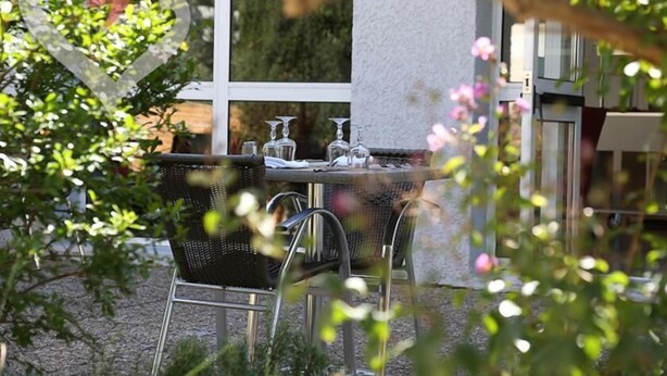 An outdoor dining area with a round table and chairs, surrounded by greenery and a building facade. - hôtel olympe (Aix-en-Provence)