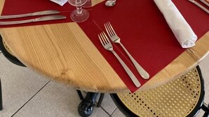 A round wooden table set for four with red placemats, clear wine glasses, silverware, and folded white napkins. - hôtel olympe (Aix-en-Provence)