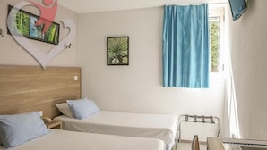 A hotel room with two beds, a wooden headboard, a small table with a chair, a TV mounted on the wall, and a window with blue curtains. - hôtel olympe (Aix-en-Provence)