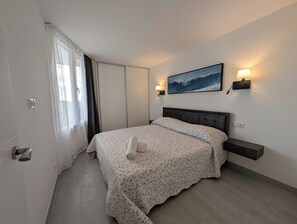 A bedroom with a bed, a nightstand, a wall-mounted lamp, and a painting of a wave. - Apartamento Lissa con vista al mar y aire condicionado (Tossa de Mar)
