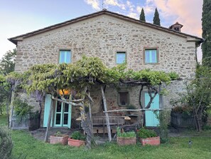 A stone house with a wooden porch, a small garden, and a bench. - Country house with pool in Anghiari Arezzo (Anghiari)