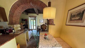 A cozy kitchen with a brick archway, a wooden table with a vase of fruit, and a hanging light fixture. - Country house with pool in Anghiari Arezzo (Anghiari)