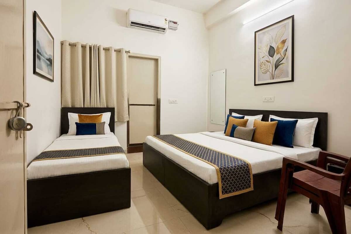 Two single beds with headboards, a wooden chair, a wall-mounted air conditioner, and a framed botanical print.