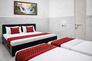 A hotel room with a bed, a bedside table, a wall-mounted painting, and a door. - Yamuna Dham (Mathura)