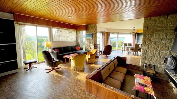 A spacious living area with a stone wall, wooden ceiling, and large windows offering a view. - House with panoramic view of the Etel ria (Belz)