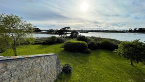 A grassy area with a stone wall, a body of water, and a bridge in the distance. - House with panoramic view of the Etel ria (Belz)