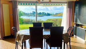 A dining area with a table and chairs, a view of a body of water, and a kitchen area with cabinets. - House with panoramic view of the Etel ria (Belz)