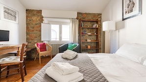 Hotellihuone, jossa on sänky, työpöytä, tuoli, patteri, kirjahylly ja ikkuna.