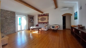 Ein geräumiges Wohnzimmer mit Holzböden, einer Steinwand, einem weißen Sofa, einem Holztisch, einem Hängekorbstuhl und einer Wanddekoration.