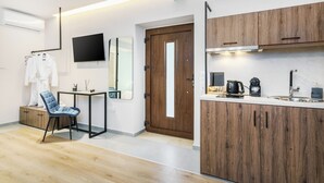Ett modernt hotellrum med trägolv, ett litet bord med en stol, en tv som är monterad på väggen, en trädörr och ett litet kök med en kaffebryggare.