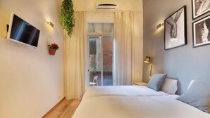 Ein Schlafzimmer mit Bett, Fernseher, einer Topfpflanze und Blick ins Freie.