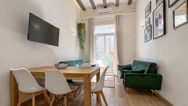 Ein modernes Wohnzimmer mit einem Holzesstisch, weißen Stühlen, einem grünen Sofa und einem flachbildfernseher an der Wand.