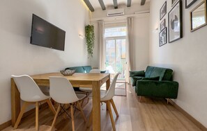 Ein modernes Wohnzimmer mit einem Holzesstisch, weißen Stühlen, einem grünen Sofa und einem flachbildfernseher an der Wand.