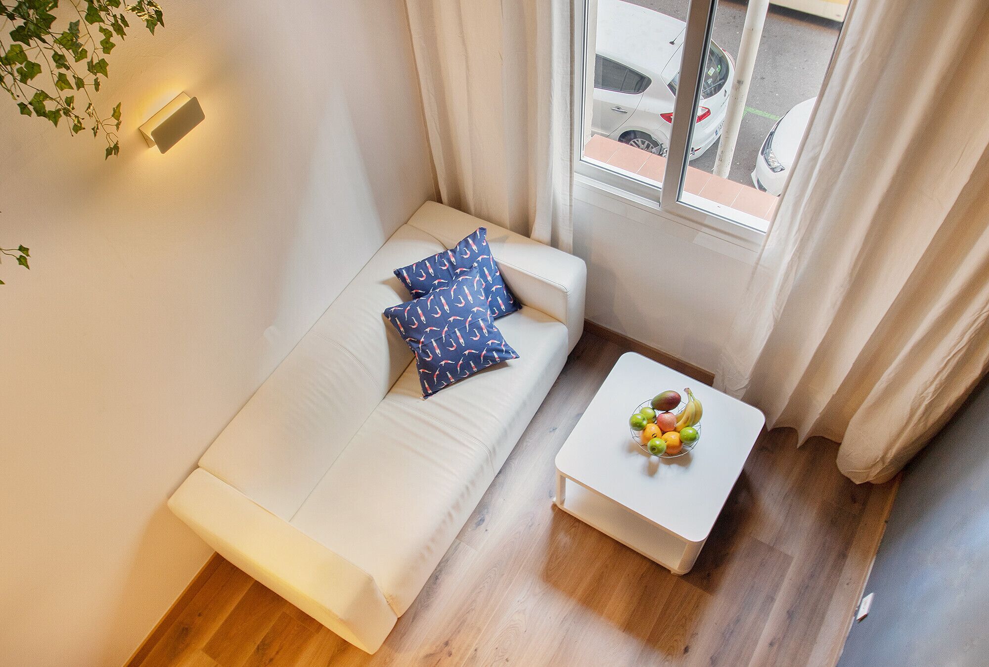 A small, cozy room with a sofa, a coffee table with fruit, and a window with curtains.
