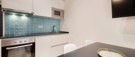 Een moderne keuken met een magnetron, oven en een blauwe betegelde spatwand. Er is een zwart aanrecht en een tafel met een gouden dienblad.