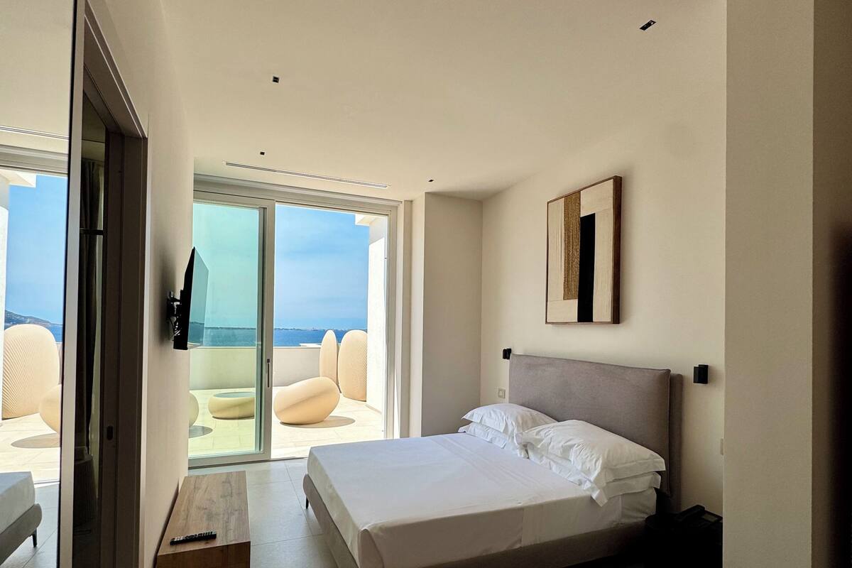 Une chambre à coucher moderne avec un grand lit, une porte-fenêtre coulissante donnant sur un balcon et un design minimaliste.