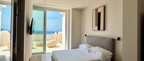 A modern bedroom with a large bed, a sliding glass door to a balcony, and a minimalist design.