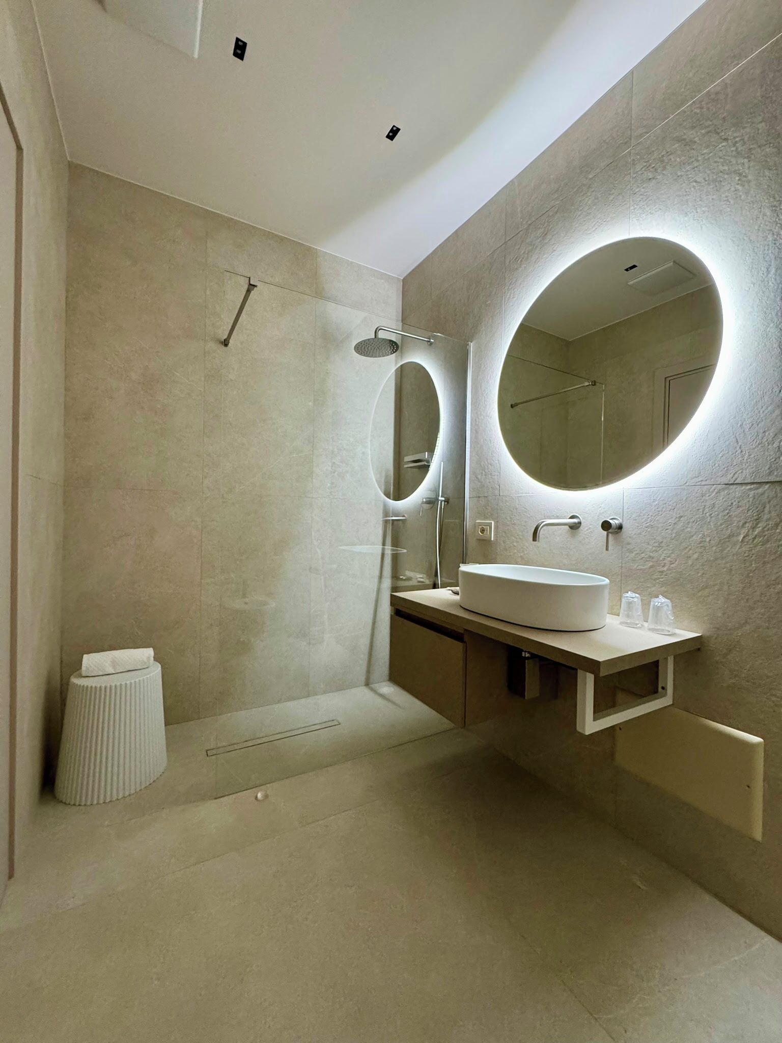 A modern bathroom with a large mirror, a round sink, and a shower.