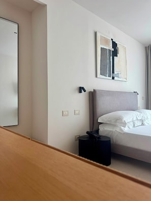 Habitación de hotel con una cama, una mesita de noche con teléfono, una lámpara de pared y un cuadro.