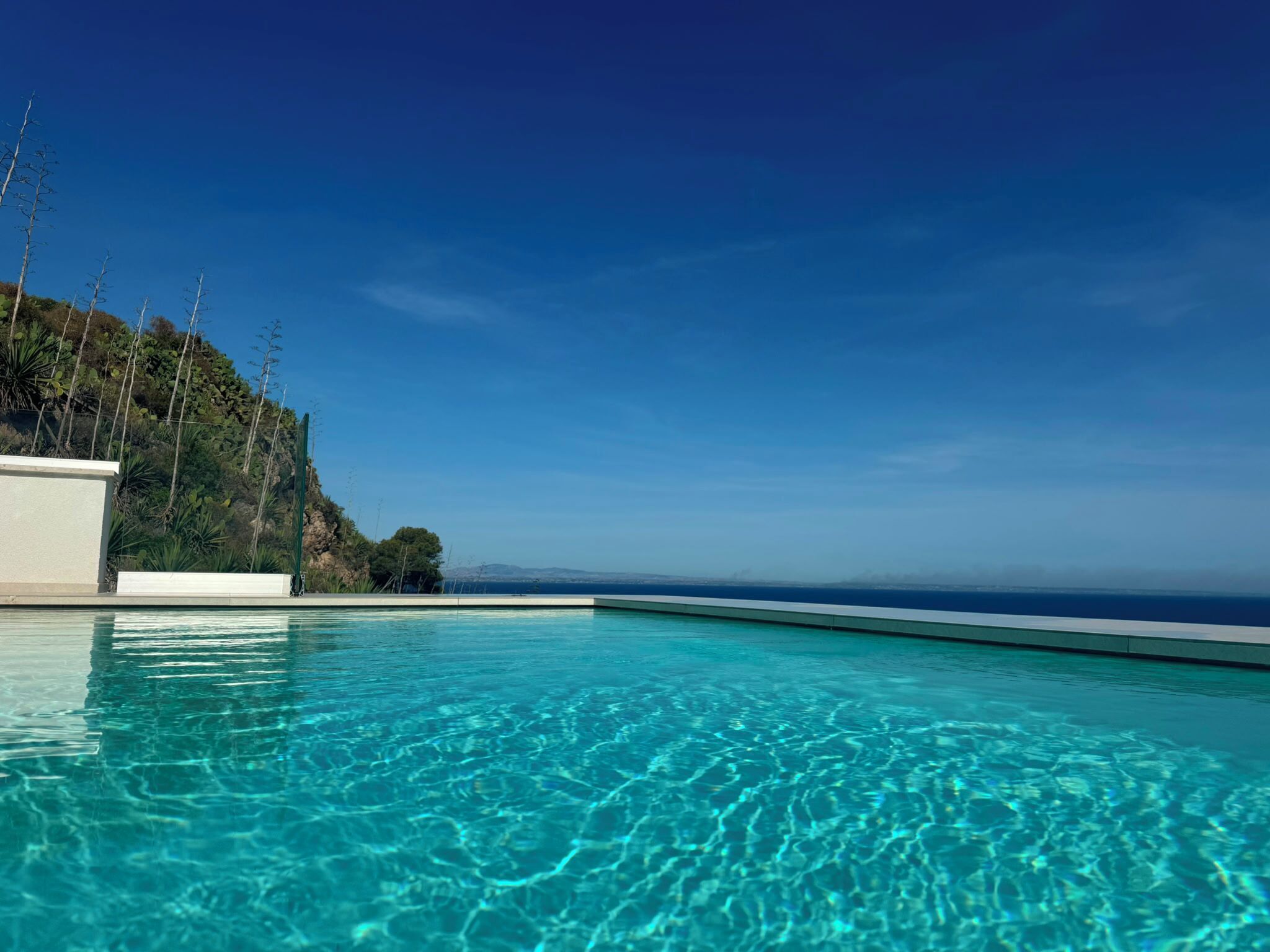 Una piscina cristalina con vistas al océano y una colina.