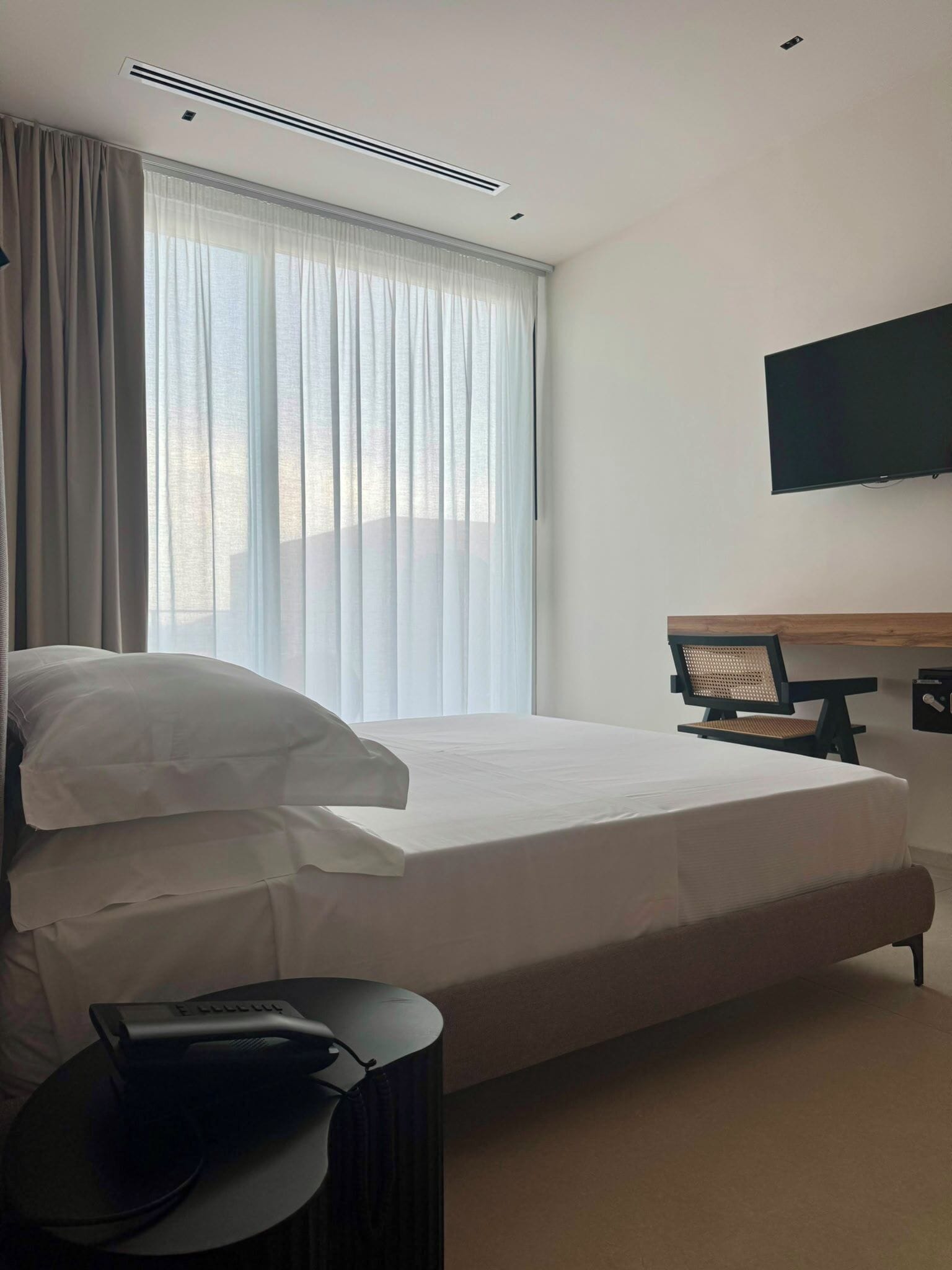 A hotel room with a bed, a desk, a chair, a TV, and a window with curtains.